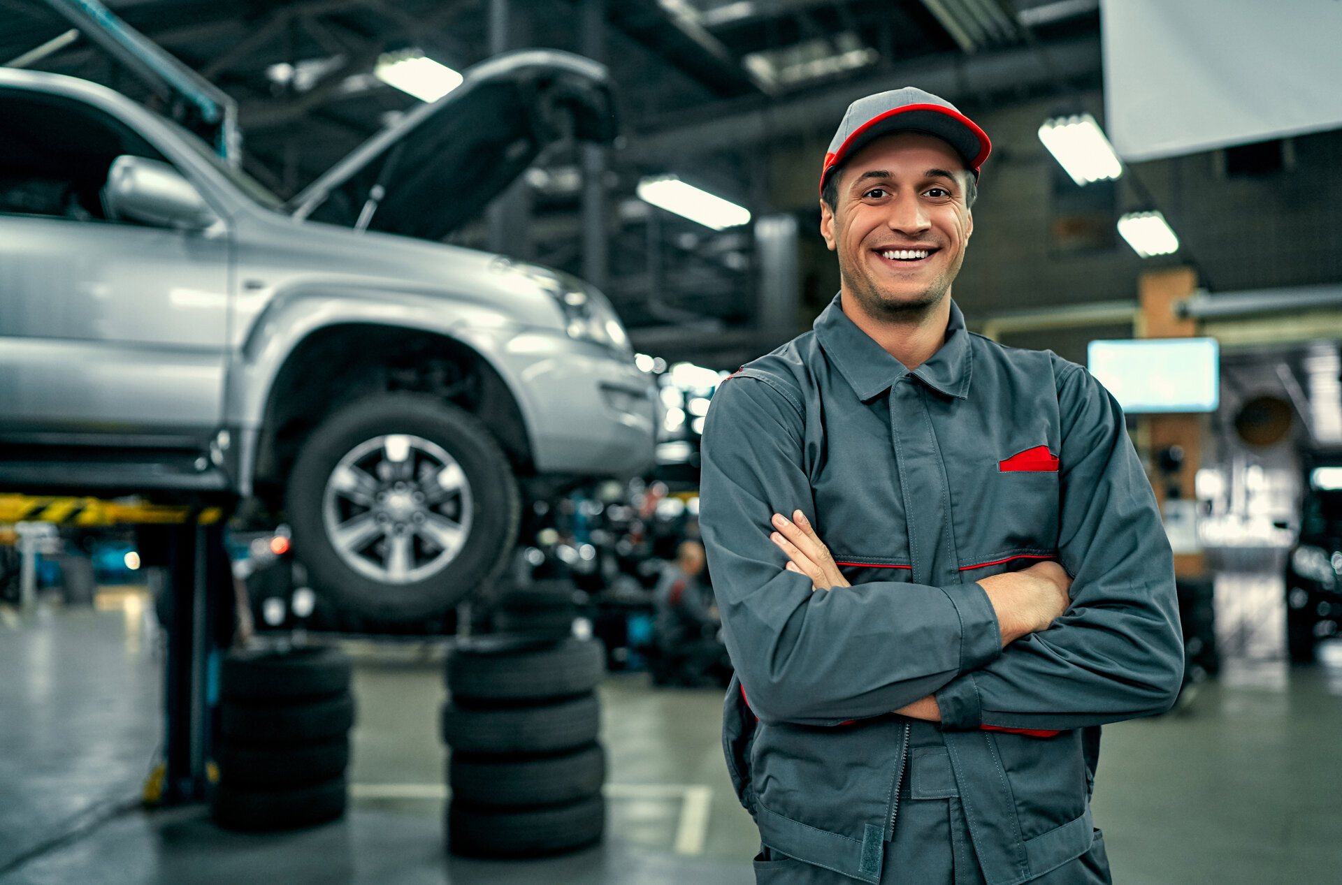 Auto-Service-Mechaniker in Uniform steht auf dem Hintergrund des Autos mit offenen Motorhaube, lächelnd und Blick auf die Kamera. Autoreparatur und Wartung.