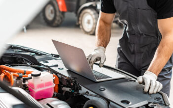 Ausschnitt eines Mechanikers, der einen Laptop in der Nähe des Motorraums eines Autos benutzt