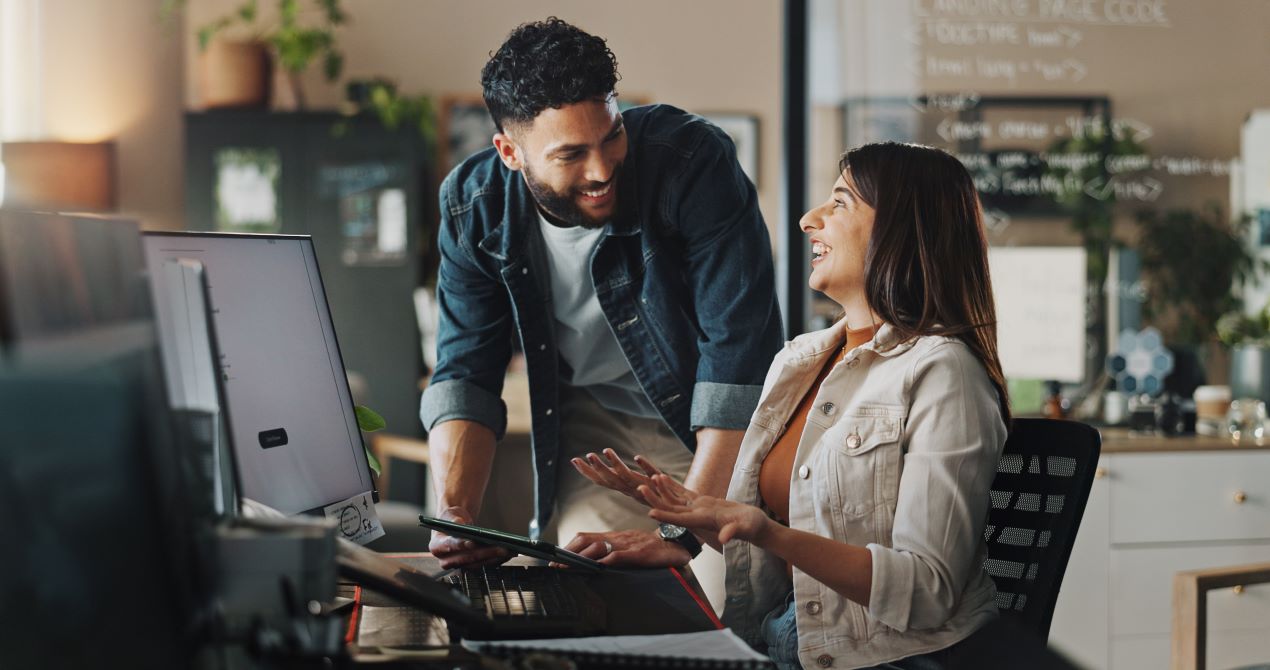 Zwei Kollegen lächeln und tauschen sich am Arbeitsplatz aus, Beispiel für die Wirkung von EmployeeAssistanceProgram.