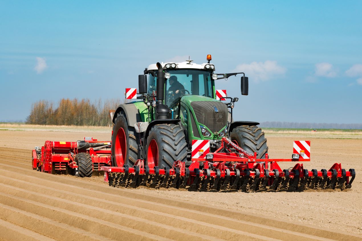 Ein moderner Traktor zieht eine Bodenfräse über ein Feld und lockert den Boden für die Aussaat.