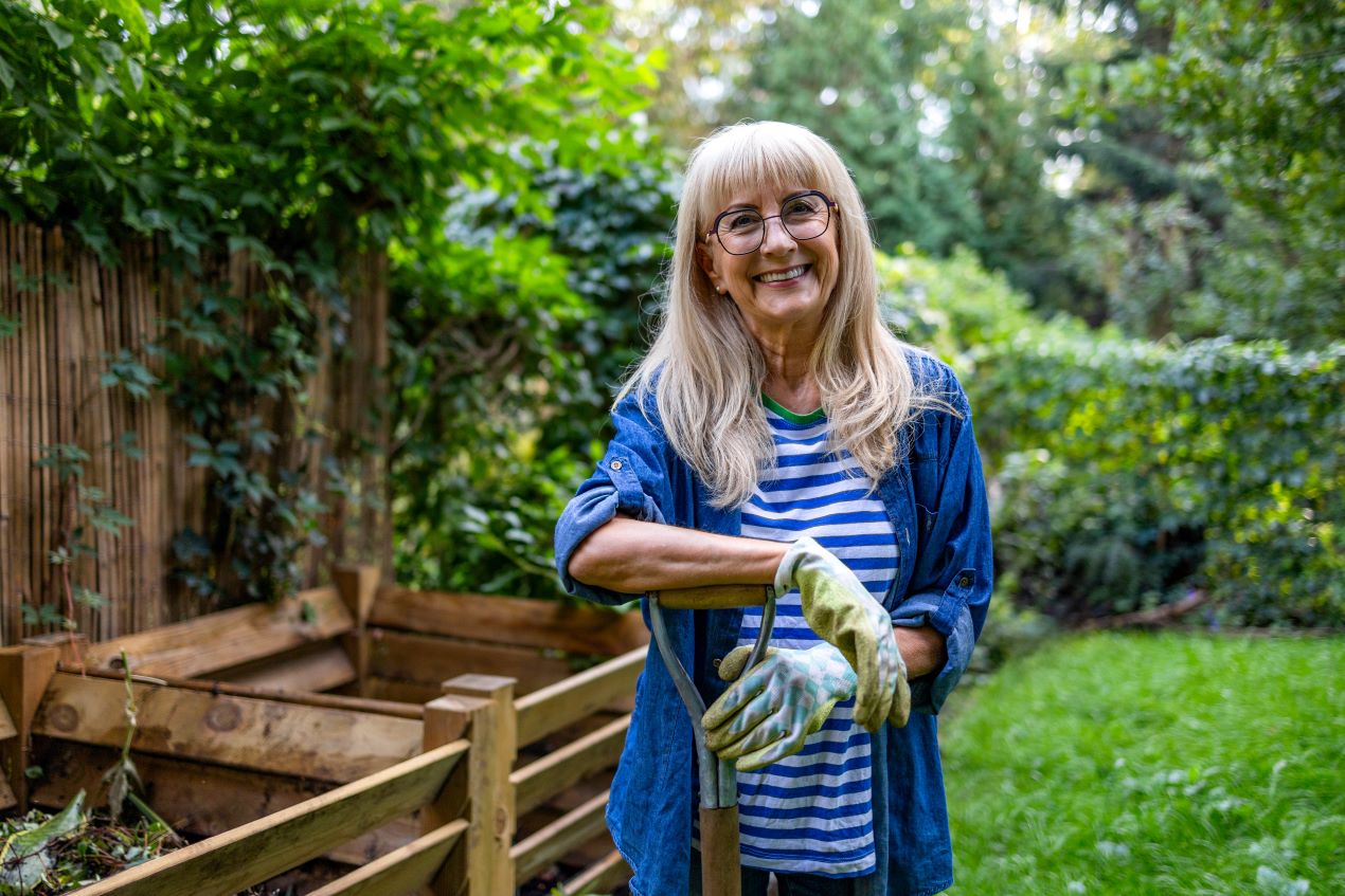 Eine lächelnde Frau in einem grünen Garten hält ein Gartenwerkzeug in der Hand, nach erfolgreicher Bodenbearbeitung mit einer Bodenfräse.