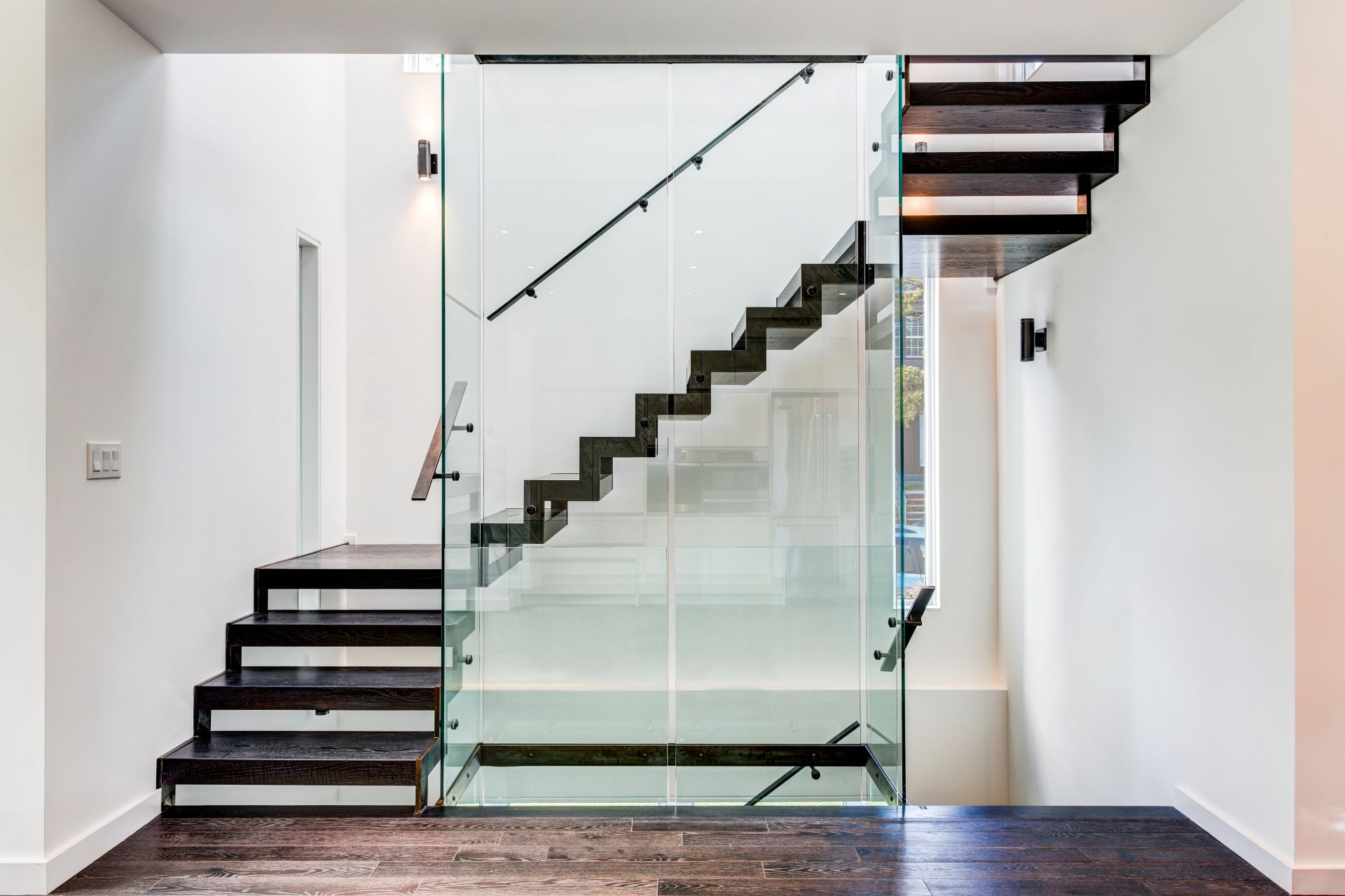 Moderne Treppe aus dunklem Holz und Glasgeländer in heller Wohnung, Beispiel für stilvolles Wohndesign beim Treppen kaufen