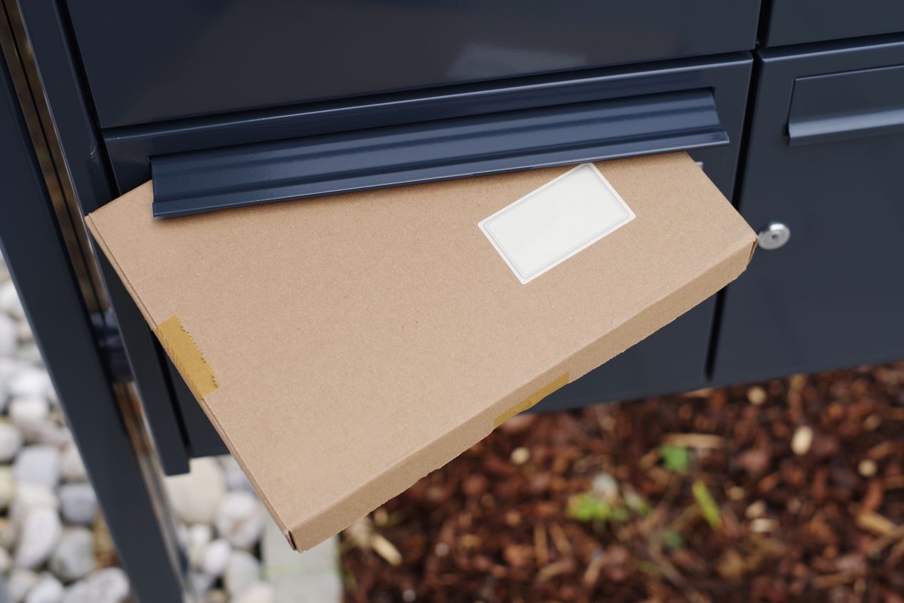 Paket wird in modernen Paketbriefkasten eingeworfen, wetterfeste Zustellung vor dem Haus