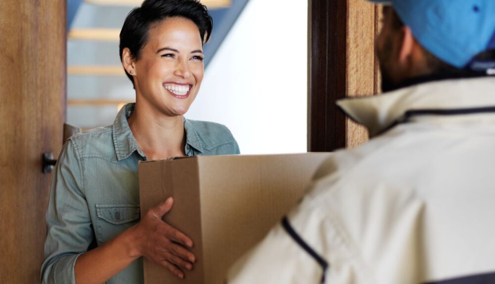 Frau nimmt Paket von Zusteller entgegen und lacht, sicherer Empfang dank Paketbriefkasten